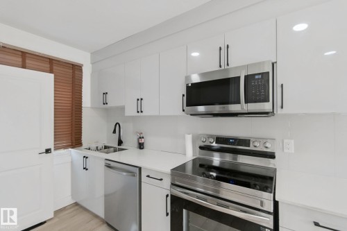 Modern kitchen featuring white cabinetry, stainless steel appliances, a black gooseneck faucet, light countertops, and wood-finish blinds - 11914 124 Street Nw, Edmonton, AB 