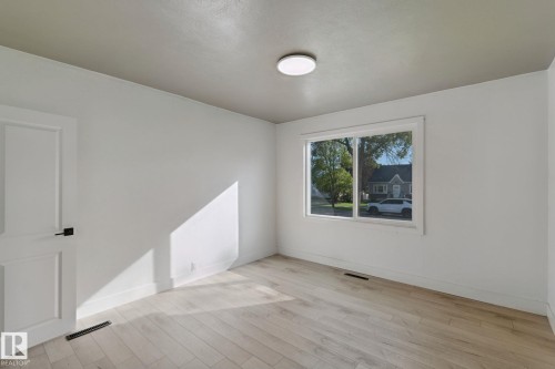 Light-colored wood-finish flooring, white walls, and a flat panel door with matte black hardware - 11914 124 Street Nw, Edmonton, AB 