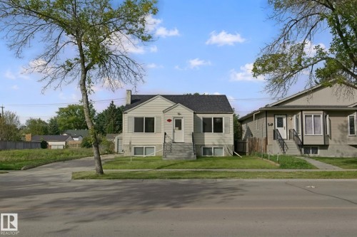 Single-family residence with light-colored siding, a dark shingled roof, a paved driveway, and a front yard with mature trees - 11914 124 Street Nw, Edmonton, AB 