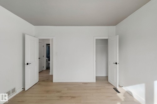 Light wood-finish flooring with white baseboards, solid white doors featuring matte black hardware, and an open closet - 11914 124 Street Nw, Edmonton, AB 