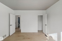Light wood-finish flooring with white baseboards, solid white doors featuring matte black hardware, and an open closet - 