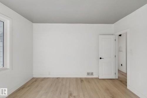Light wood-finish flooring, white walls, white trim, and a white interior door with black hardware - 11914 124 Street Nw, Edmonton, AB 