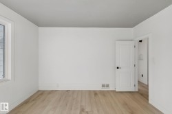 Light wood-finish flooring, white walls, white trim, and a white interior door with black hardware - 