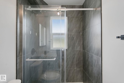 Frameless glass shower enclosure with a sliding barn door, dark grey tile surround, built-in shower niche, and a window - 11914 124 Street Nw, Edmonton, AB 