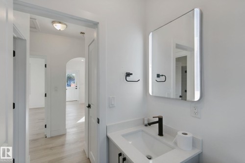 Modern bathroom vanity with a white countertop and rectangular undermount sink, complemented by a black faucet and built-in lighting in the mirror - 11914 124 Street Nw, Edmonton, AB 