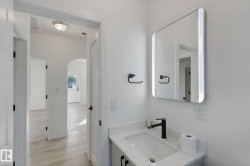 Modern bathroom vanity with a white countertop and rectangular undermount sink, complemented by a black faucet and built-in lighting in the mirror - 