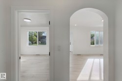 Archway entry into a bright space with wood-finish flooring and white walls - 