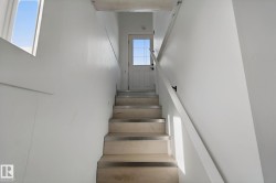 Staircase featuring light wood treads with metal accents, white walls, and a window - 