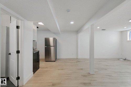 Spacious room with light wood-finish flooring, recessed lighting, and a stainless steel refrigerator - 11914 124 Street Nw, Edmonton, AB 
