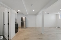 Spacious room with light wood-finish flooring, recessed lighting, and a stainless steel refrigerator - 