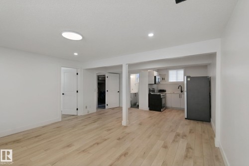 Open-concept space featuring wood-finish flooring, recessed lighting, and a kitchen area with light-toned cabinetry and a black refrigerator - 11914 124 Street Nw, Edmonton, AB 
