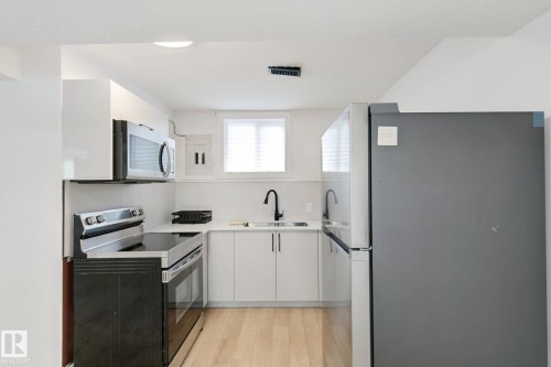 Kitchen featuring stainless steel appliances, white cabinetry, light-toned wood-finish flooring, and a window with blinds - 11914 124 Street Nw, Edmonton, AB 