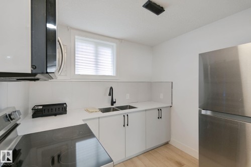 Modern kitchen featuring stainless steel appliances, white cabinetry with matte black hardware, white countertops, and wood-finish flooring - 11914 124 Street Nw, Edmonton, AB 