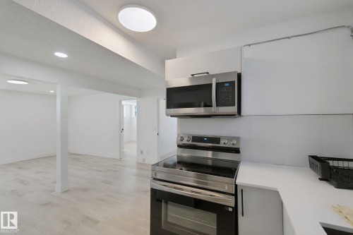 Stainless steel range and microwave, white cabinetry, solid surface countertop, and wood-finish flooring - 11914 124 Street Nw, Edmonton, AB 