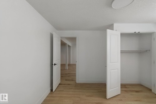 Wood-finish flooring, white walls, and a closet with bi-fold doors and integrated shelving - 11914 124 Street Nw, Edmonton, AB 