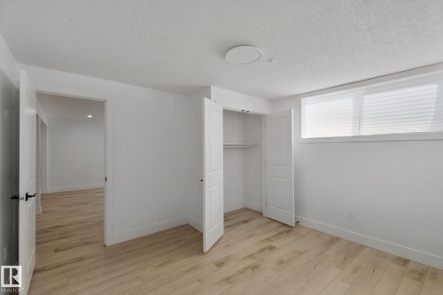 Wood-finish flooring, white walls, built-in closet with bifold doors, window with horizontal blinds, and a flush-mount ceiling light - 11914 124 Street Nw, Edmonton, AB 