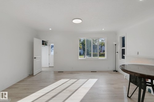 Spacious room featuring light wood-finish flooring, white walls, multiple windows, recessed lighting, and a flush-mount ceiling light fixture - 11914 124 Street Nw, Edmonton, AB 