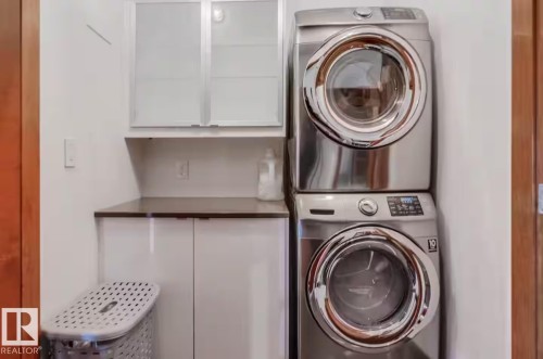 Stackable stainless steel washer and dryer, white cabinetry, dark countertop, and upper cabinets with frosted glass inserts - #701 10105 109 St Nw, Edmonton, AB 