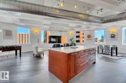Contemporary open-concept living space featuring an expansive kitchen island with a light-toned countertop, wood-finish flooring, and exposed spiral ductwork - 