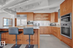 Kitchen featuring light wood cabinetry, stainless steel appliances, a white tile backsplash, a large island with a white countertop, and exposed ductwork - 