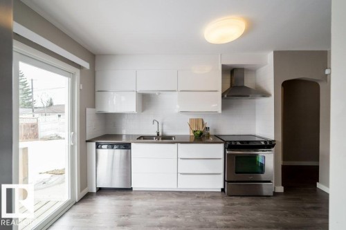 Kitchen featuring stainless steel appliances, white flat-panel cabinetry, a subway tile backsplash, and wood-finish flooring - 12228 134 Street Nw, Edmonton, AB 