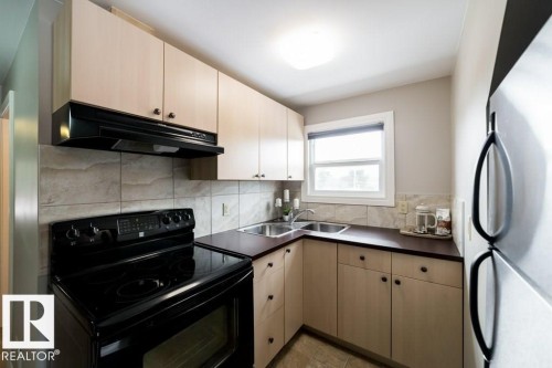 Kitchen featuring light-tone cabinetry, a dual basin stainless steel sink, black electric range with overhead ventilation, and a window with white trim - 12228 134 Street Nw, Edmonton, AB 