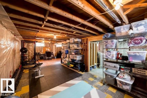 Unfinished basement featuring exposed wood joists, partial wall framing, and a dedicated area with wood-finish flooring - 12228 134 Street Nw, Edmonton, AB 
