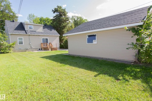 Expansive grassy area, detached garage with beige siding, main residence featuring beige siding, wooden deck, and a dormer window - 12228 134 Street Nw, Edmonton, AB 