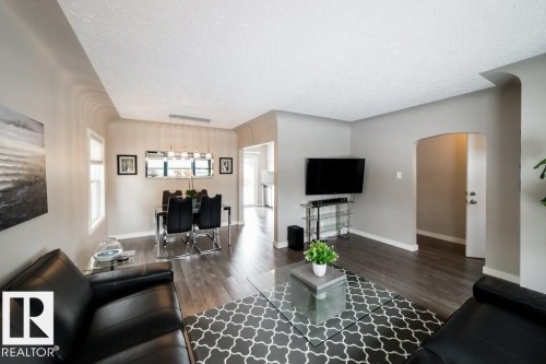 Open-concept living area with wood-finish flooring, a dining space with a linear pendant light, and an arched doorway - 12228 134 Street Nw, Edmonton, AB 