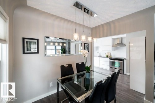 Dining area with a multi-pendant linear chandelier, a sleek glass-top table, and wood-finish flooring - 12228 134 Street Nw, Edmonton, AB 