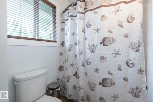 Bathroom featuring a white toilet, light blue wall paint, and a window with wood-finish blinds - #20 3812 20 Av Nw, Edmonton, AB 