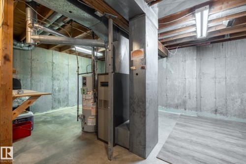 Unfinished basement featuring exposed wood beams, concrete walls, a water heater, furnace, and a section of wood-finish flooring - #20 3812 20 Av Nw, Edmonton, AB 