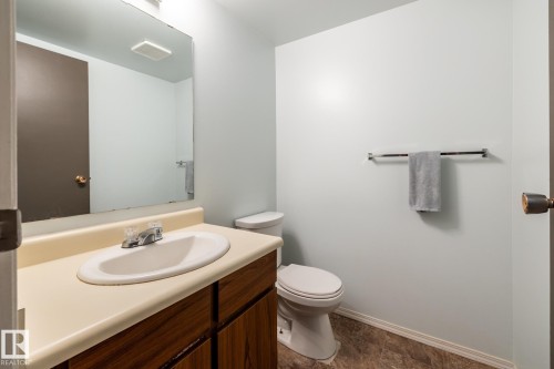 Bathroom featuring a wood-finish vanity with an integrated sink, a large wall-mounted mirror, and a toilet - #20 3812 20 Av Nw, Edmonton, AB 