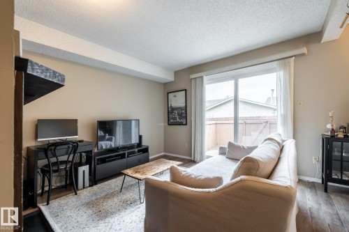 Living area featuring wood-finish flooring, light neutral wall tones, and a sliding glass door providing access to an outdoor patio space - #20 3812 20 Av Nw, Edmonton, AB 