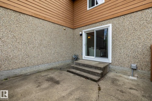 Sliding glass door entry from a concrete patio, featuring a wood-paneled upper exterior and textured stucco lower exterior - #20 3812 20 Av Nw, Edmonton, AB 