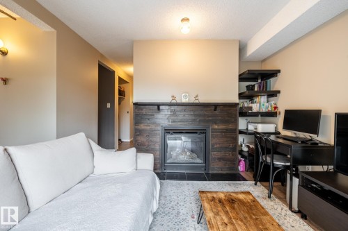 Central fireplace with dark wood-finish surround and black tile hearth - #20 3812 20 Av Nw, Edmonton, AB 