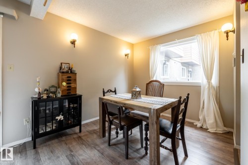 Bright room featuring wood-finish flooring, a large window with white curtains, and two wall sconces providing ambient lighting - #20 3812 20 Av Nw, Edmonton, AB 