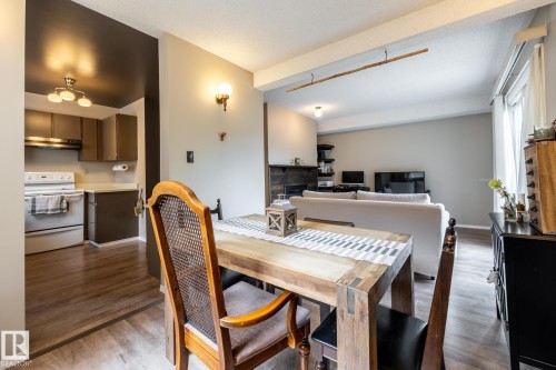 Open-concept living space featuring wood-finish flooring, a rustic wood dining table, and a kitchen with brown cabinetry and white appliances - #20 3812 20 Av Nw, Edmonton, AB 