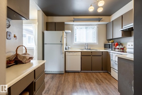Kitchen featuring wood-finish flooring, white appliances, and a window above the sink - #20 3812 20 Av Nw, Edmonton, AB 