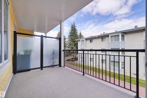 Balcony with black metal railings, a textured concrete floor, and frosted privacy screens - #215 9820 165 St Nw, Edmonton, AB 
