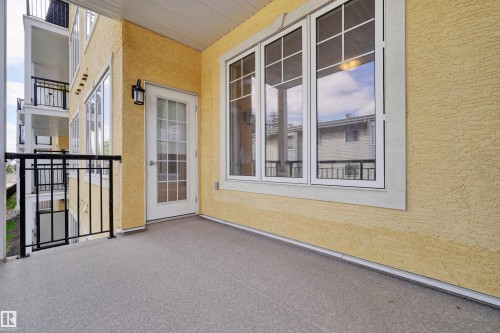 Private balcony with textured stucco exterior, white-framed windows, and a glass-paneled door - #215 9820 165 St Nw, Edmonton, AB 