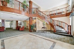 Expansive foyer featuring a grand curved staircase with wrought iron and wood railings, tile flooring with decorative inlay, patterned carpet, and built-in lighting - 