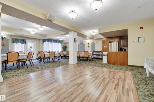 Expansive gathering space featuring wood-finish flooring, patterned carpeting, multiple sets of double windows, and a built-in refreshment bar with stainless steel appliances - #215 9820 165 St Nw, Edmonton, AB 