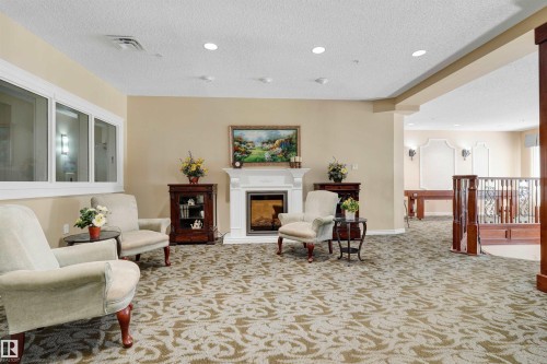 Recessed lighting, white fireplace with mantle, large windows, patterned carpet, and wood-toned railing - #215 9820 165 St Nw, Edmonton, AB 