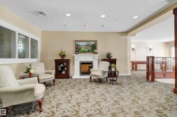 Recessed lighting, white fireplace with mantle, large windows, patterned carpet, and wood-toned railing - 