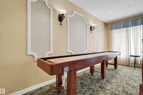 Recessed lighting, decorative wall sconces, wall paneling, patterned carpeting, and a built-in shuffleboard table - #215 9820 165 St Nw, Edmonton, AB 