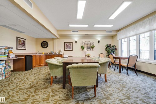 Expansive room featuring patterned carpet, recessed lighting, a built-in wet bar with wood cabinetry, and large windows - #215 9820 165 St Nw, Edmonton, AB 