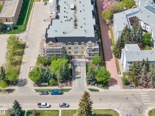 Yellow multi-story building featuring a dark shingled roof, multiple balconies, and a paved entry drive - #215 9820 165 St Nw, Edmonton, AB 