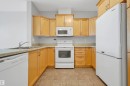 U-shaped kitchen featuring wood cabinetry, white appliances, double basin sink, and tile flooring - #215 9820 165 St Nw, Edmonton, AB 