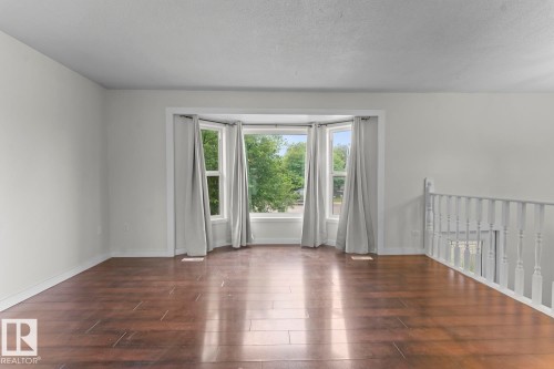 Spacious interior featuring a bay window, wood-finish flooring, white walls, white trim, and a white baluster railing - 4412 51 Avenue, Cold Lake, AB - Indoor Photo Showing Other Room
